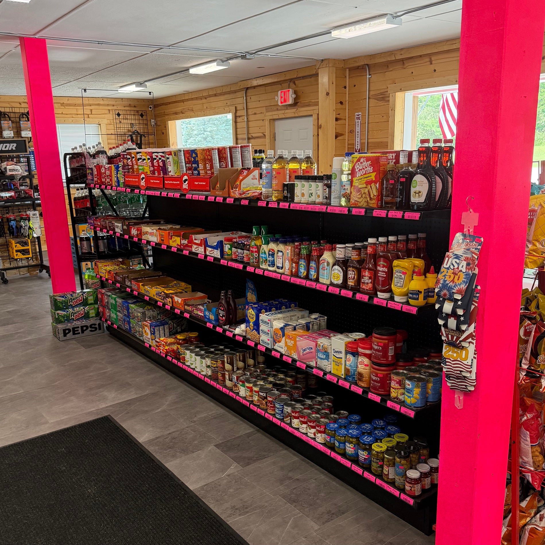 A grocery store aisle with black shelving stocked with bottled beverages, canned goods, and packaged snacks.